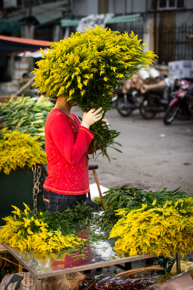 Yellow flowers cover the face of a flower seller in the Quang Ba