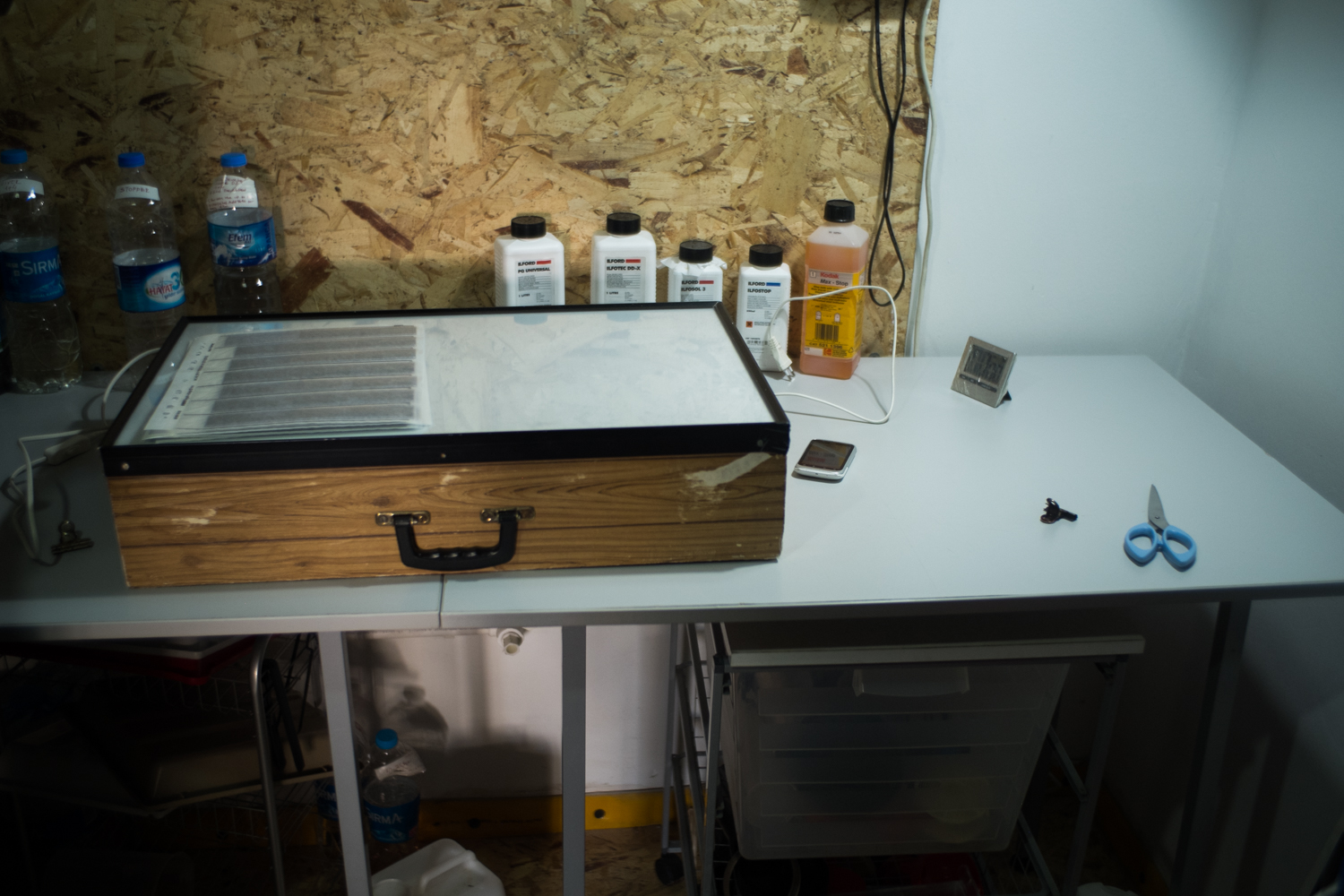 A worktable with bottles, a closed wooden box, scissors, a phone, and small tools in a corner workspace.