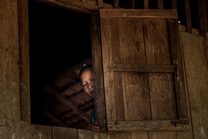 A girl peeks out the window of her wooden home in the extremely remote village of Pare-Ou, situated beside the Salawin river which divides Northwestern Thailand from Myanmar.