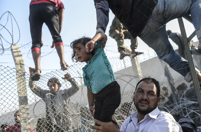 A Syrian child fleeing the war is lifted over border fences to enter Turkish territory illegally, near the Turkish border crossing at Akcakale in Sanliurfa province on June 14, 2015. Turkey said it was taking measures to limit the flow of Syrian refugees onto its territory after an influx of thousands more over the last days due to fighting between Kurds and jihadists. Under an "open-door" policy, Turkey has taken in 1.8 million Syrian refugees since the conflict in Syria erupted in 2011. AFP PHOTO / BULENT KILIC / AFP / BULENT KILIC