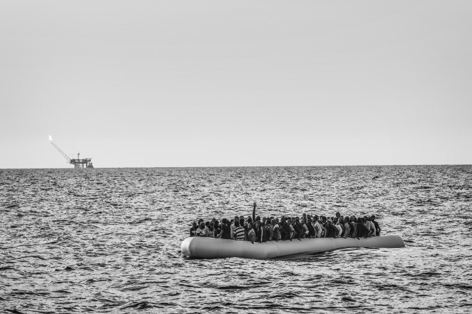 An overcrowded rubber dinghy sailed from the Libyan coast is apprached by the M.S.F. (Médecins Sans Frontières - Doctors Without Borders) search and rescue ship Bourbon Argos in the Mediterranean Sea, in international waters. The migrants on board the dinghy in distress have issued an emergency call and are waiting to be rescued. On the horizon, an offshore oil platform just off the Libyan coast. 26 August 2015. In 2015 the ever-increasing number of migrants attempting to cross the Mediterranean Sea on unseaworthy vessels towards Europe led to an unprecedented crisis. Nearly 120 thousand people have reached Italy in the first 8 months of the year. While the European governments struggled to deal with the influx, the death toll in the Mediterranean reached record numbers. Early in May the international medical relief organization Médecins Sans Frontières (M.S.F.) joined in the search and rescue operations led in the Mediterranean Sea and launched three ships at different stages: the Phoenix (run by the Migrant Offshore Aid Station), the Bourbon Argos and Dignity.