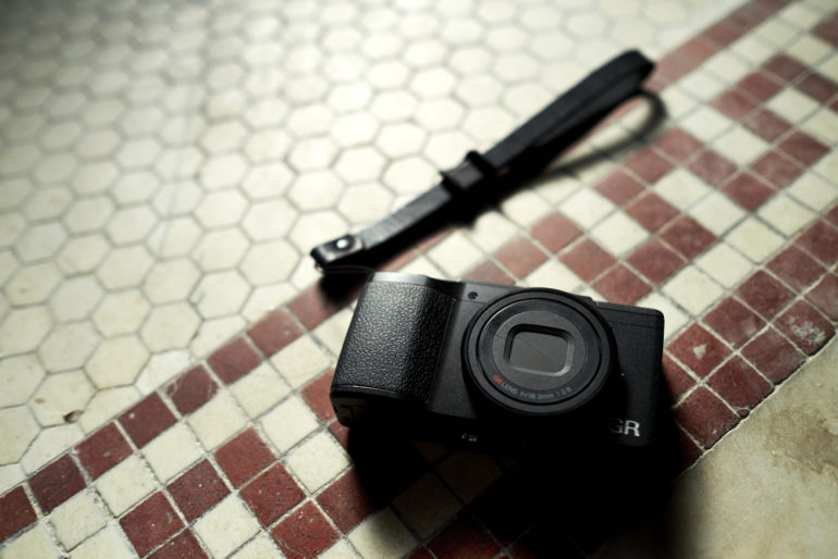 Compact black camera with a wrist strap on tiled floor.