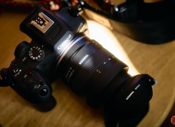 A Canon camera with a Tamron lens rests on a wooden surface under warm lighting.