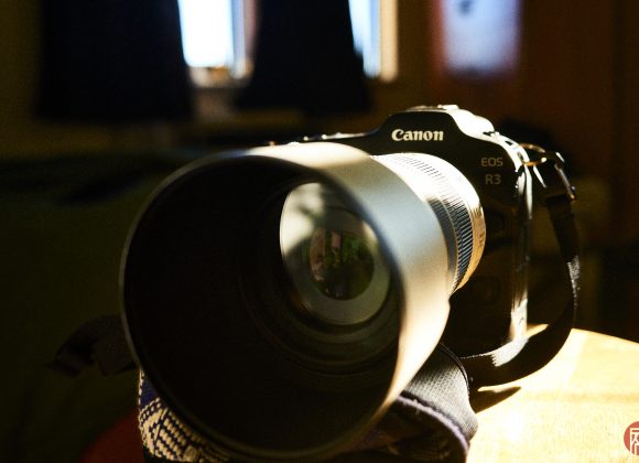 Close-up of a Canon EOS R3 camera with a large telephoto lens, placed on a table in a sunlit room.