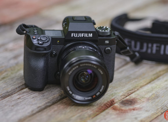 A black Fujifilm camera with a lens and strap rests on a wooden surface.