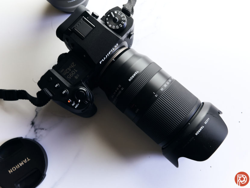 Fujifilm X-S20 camera with a Tamron 18-300mm lens on a white surface, lens cap nearby.