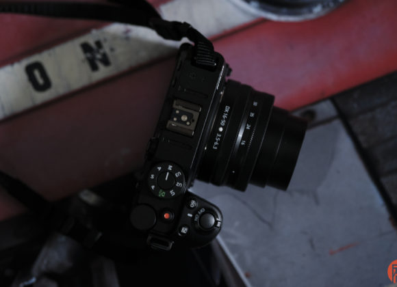 A black digital camera with a lens rests on a red and white metal surface with letters partially visible.