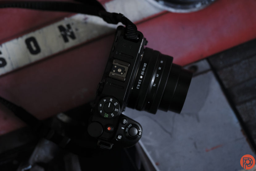 A black digital camera with a lens rests on a red and white metal surface with letters partially visible.