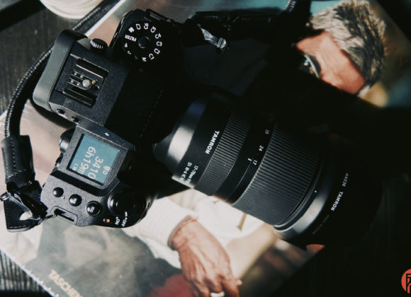 A black digital camera with a large lens rests on a magazine featuring a person in sunglasses.