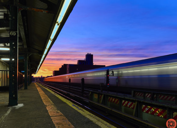 Train station at dusk with a blurred train passing by, vibrant purple and orange sky in the background.