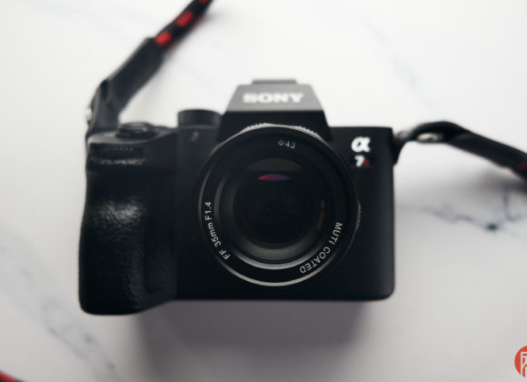 A Sony Alpha camera with a lens attached, facing forward on a white marble surface.