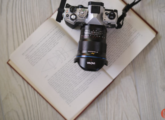 A camera rests on top of an open book with diagrams, placed on a light wood surface.