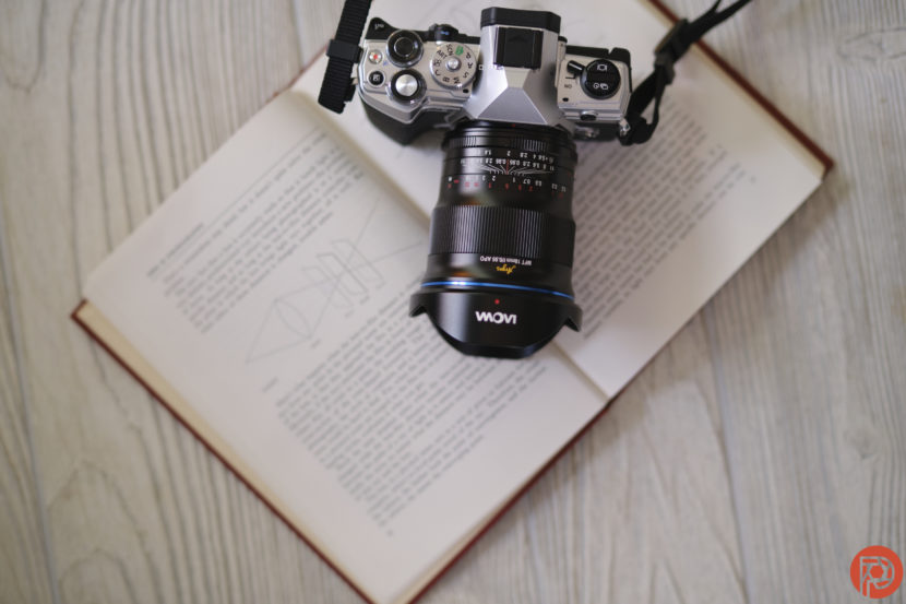 A camera rests on top of an open book with diagrams, placed on a light wood surface.