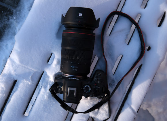 Canon camera with a zoom lens and strap resting on a snow-covered wooden surface.