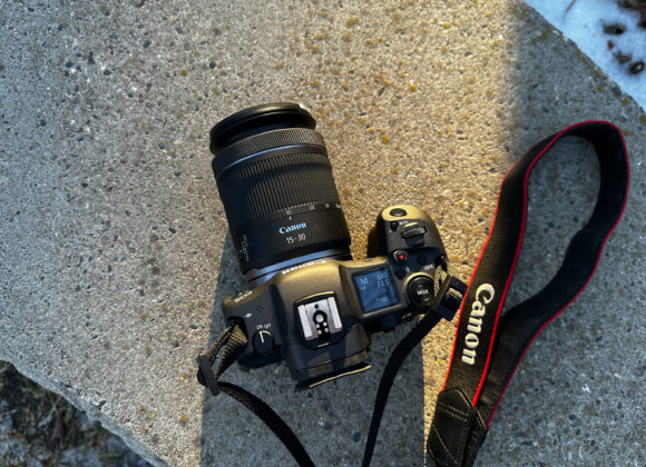 Canon camera with a 15-30mm lens and strap resting on a concrete surface in sunlight.