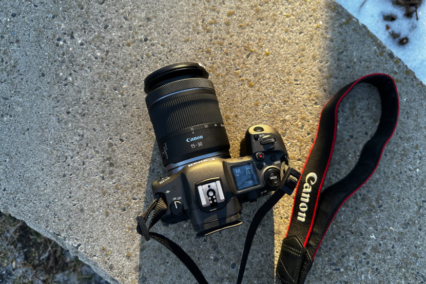 Canon camera with a 15-30mm lens and strap resting on a concrete surface in sunlight.
