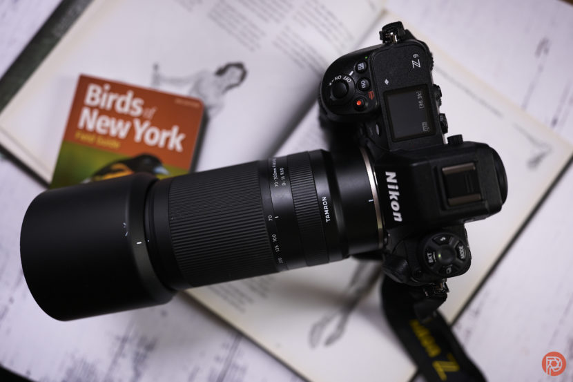 A Nikon camera with a zoom lens on an open book, next to a Birds of New York guide.