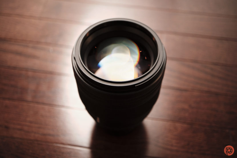 Close-up of a camera lens on a wooden floor with light reflecting off the glass elements.