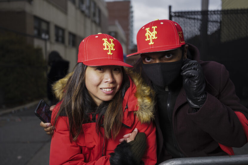 How the Right Colors in a Scene Can Affect it Differently Two people wearing red caps and jackets stand closely, one smiles and the other wears a mask, in an urban outdoor setting. Credit: Chris Gampat