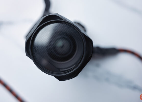 Close-up of a camera lens with a red and black strap on a white and gray surface.