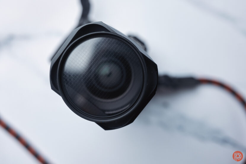 Close-up of a camera lens with a red and black strap on a white and gray surface.