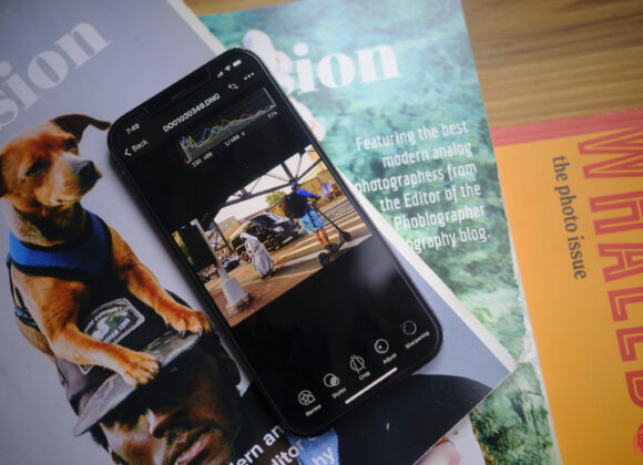 A smartphone editing a photo rests on magazines, one with a dog on the cover and another titled WHALED.