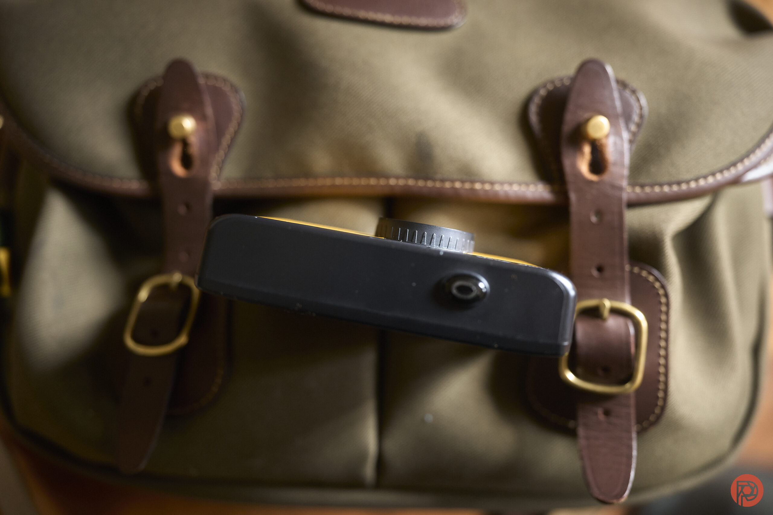 A close-up of a camera on top of a brown leather-strapped canvas bag.