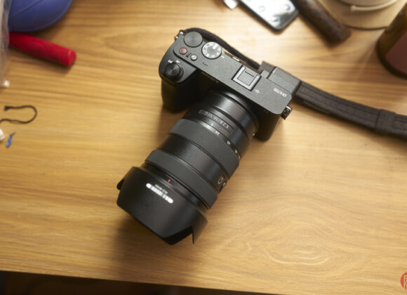 A black Sony Alpha camera with a zoom lens sits on a wooden desk among various items.