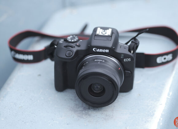 A Canon EOS camera with lens and strap resting on a light blue surface.