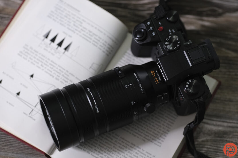 A black DSLR camera with a long zoom lens rests on top of an open technical book with diagrams.