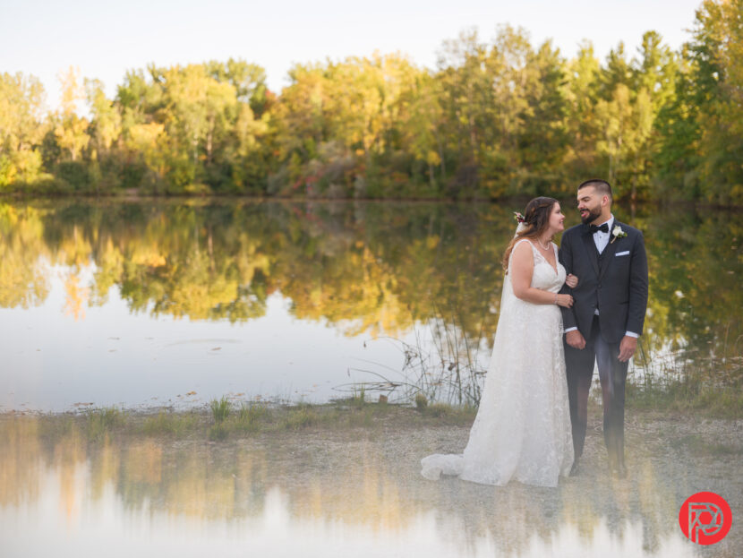 A 'Wedding Photographer' Faked His Entire Portfolio. Here's What Happened Next Bride and groom smiling by a lake with autumn trees reflected in the water.