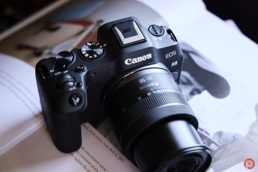 A Canon EOS R8 camera with a 24-50mm lens rests on an open magazine.