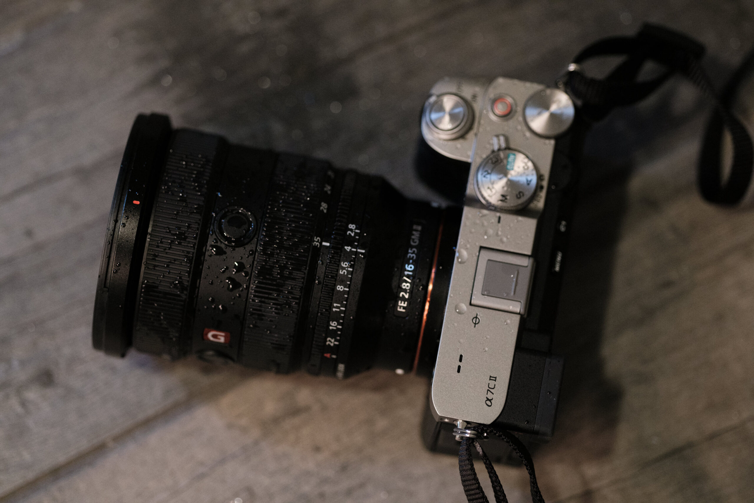 A silver camera with a black lens, covered in water droplets, rests on a wooden surface.