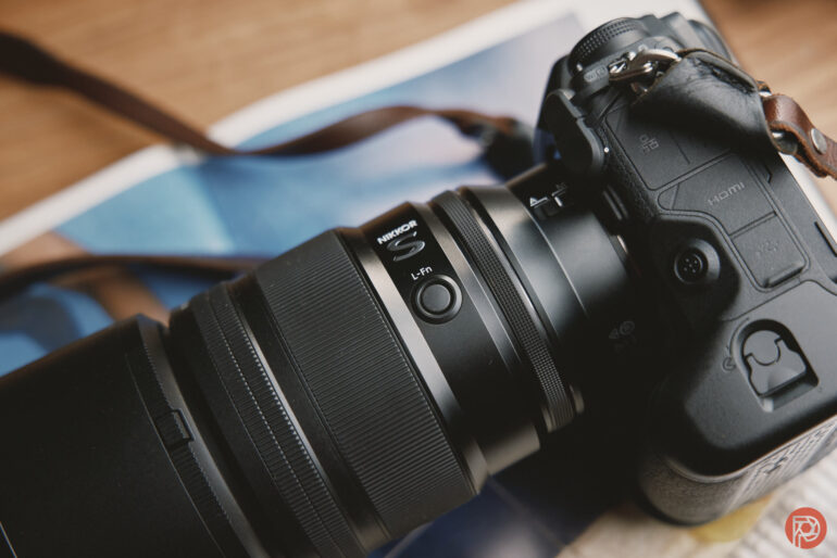 Close-up of a black Nikon camera with a zoom lens resting on a surface with a blurred background.