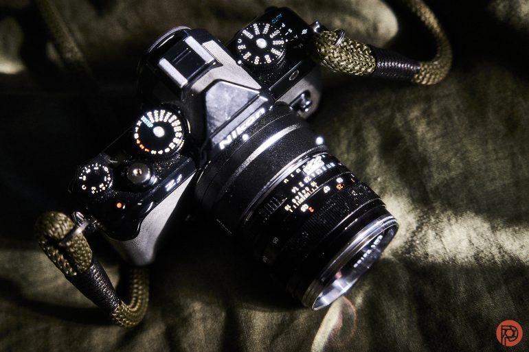 A vintage Nikon film camera with a green paracord strap rests on a dark green fabric surface.