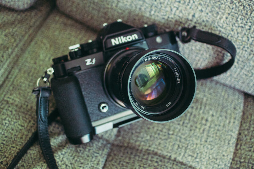 A Nikon Z f camera with a lens attached rests on a textured gray fabric surface.