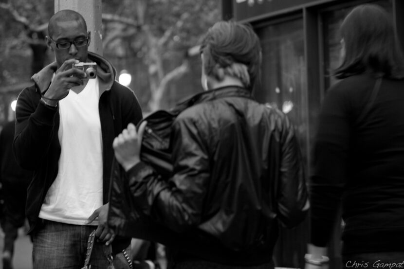 Man taking a photo on a street as a person adjusts their jacket.