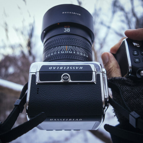 Close-up of a person holding a Hasselblad camera outdoors in winter, with trees blurred in the background.