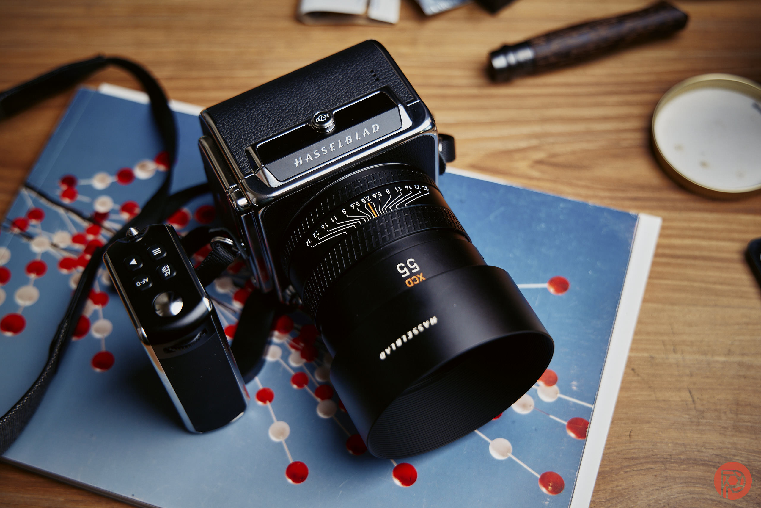 A Hasselblad camera rests on a blue notebook with a molecular diagram on a wooden table.