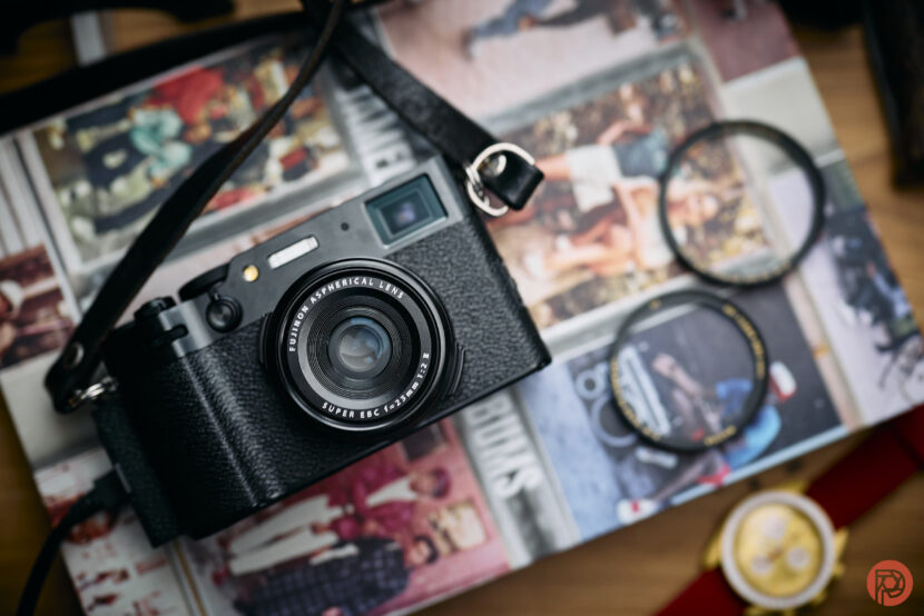 A black camera with a lens rests on an open magazine, with filters and a watch nearby.