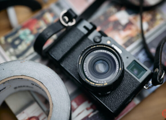 Vintage Fujifilm camera with a lens, surrounded by duct tape and a blurred colorful background.