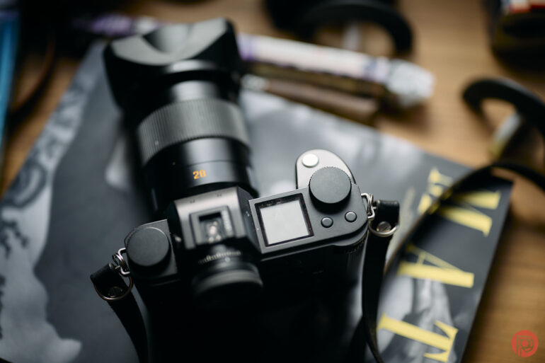 A black digital camera with a large lens rests on a partially visible magazine on a wooden surface.