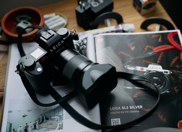 A Leica camera rests on an open magazine featuring a Leica SL2 Silver camera advertisement.