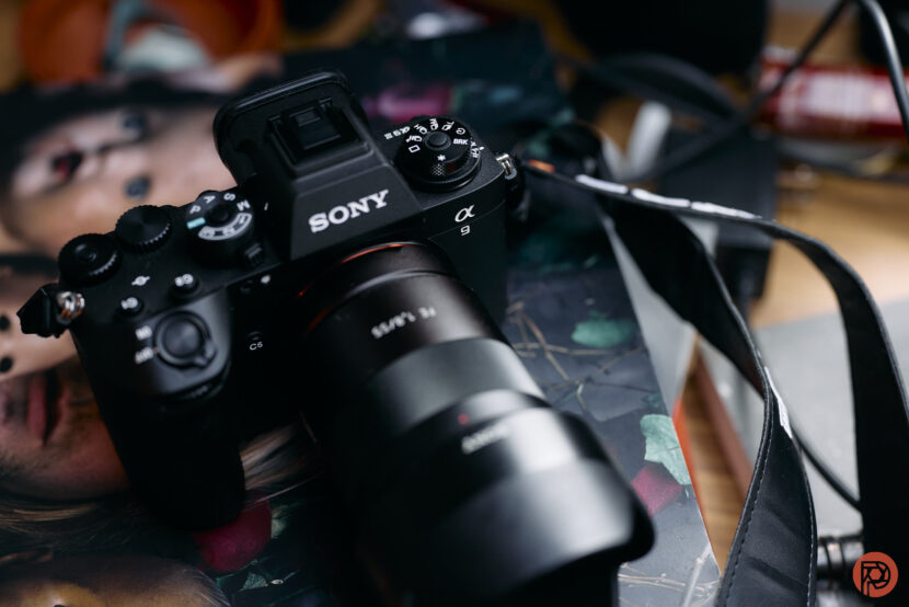 A Sony Alpha camera with a lens attached rests on a colorful magazine on a cluttered desk.