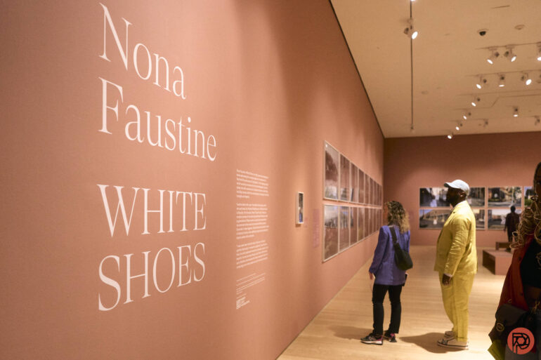 Two people view the “Nona Faustine: White Shoes” exhibit in a pink-walled art gallery.