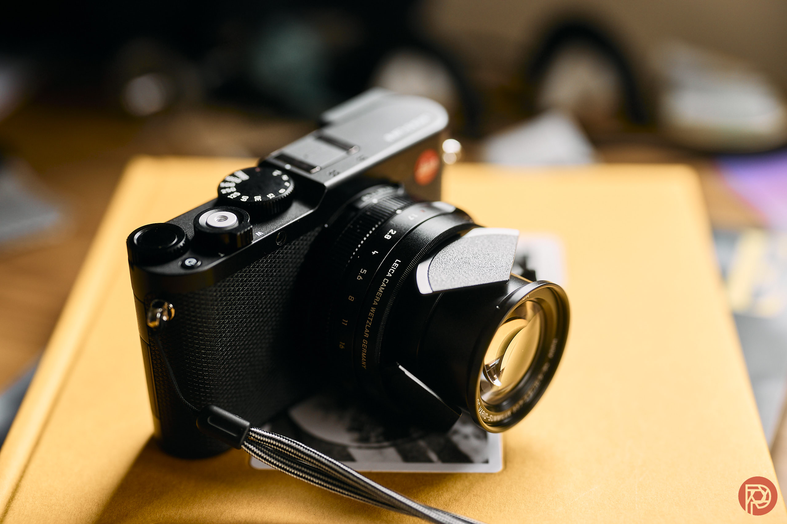 A black Leica camera rests on a closed yellow notebook with a blurred background.
