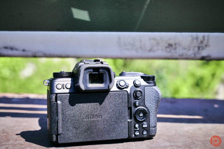 A black Nikon camera is placed outdoors on a wooden surface in bright sunlight.