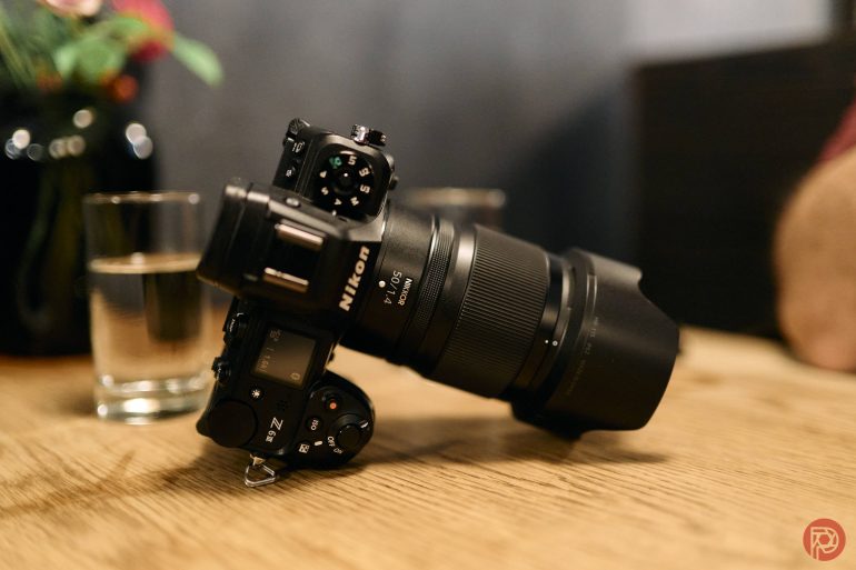 A black Nikon camera with a large lens rests on a wooden table near a glass of water.