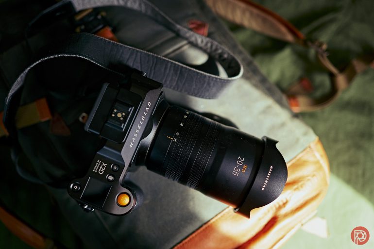 A Hasselblad camera with a wide lens rests on a gray and brown camera bag.