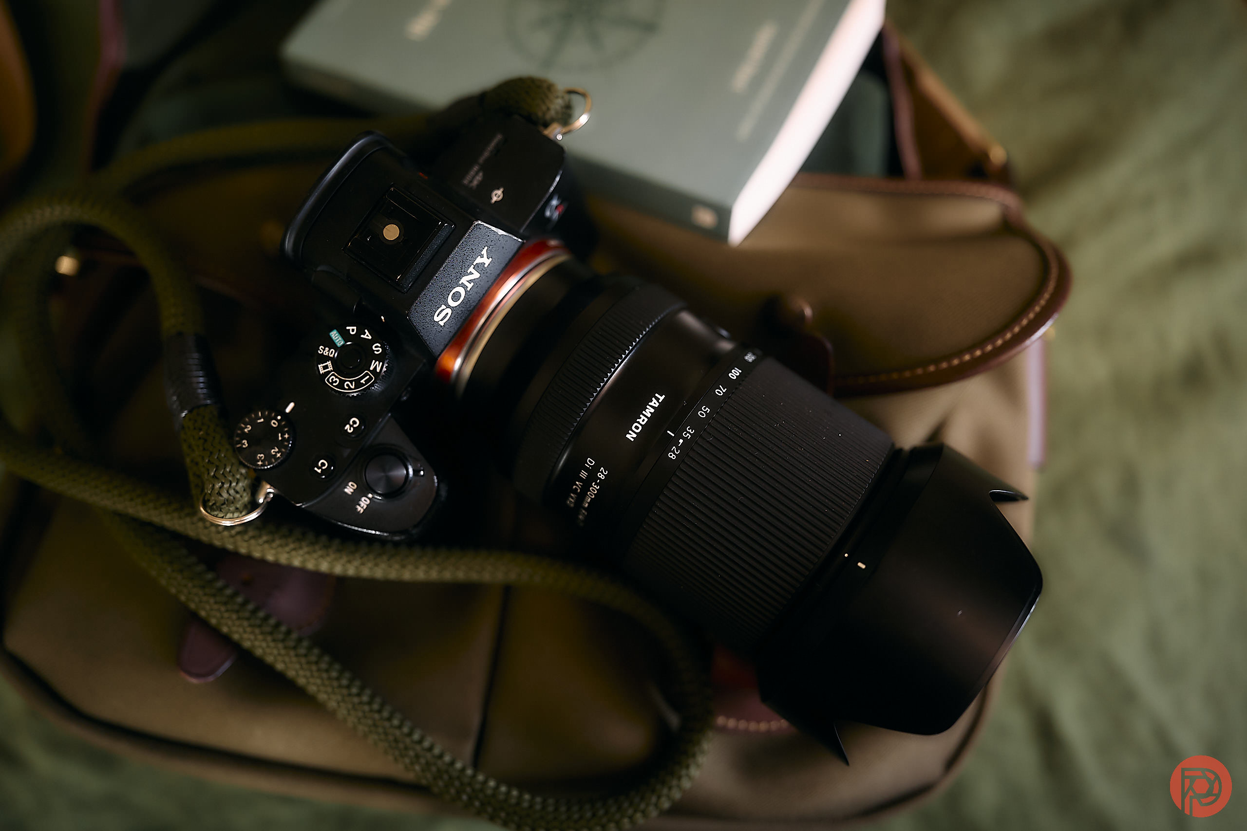 Sony camera with Tamron lens rests on a tan bag, with a green book partially visible in the background.